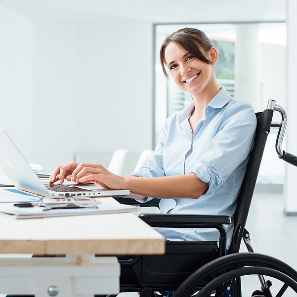 Confident happy businesswoman in wheelchair working at office desk and using a laptop she is smiling at camera disability overcoming concept